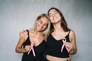 Two smiling women holding pink breast cancer awareness ribbons, symbolizing strength and support after breast reconstruction surgery.
